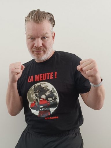 Homme souriant en t-shirt noir avec un design graphique et les mots "LA MEUTE!"